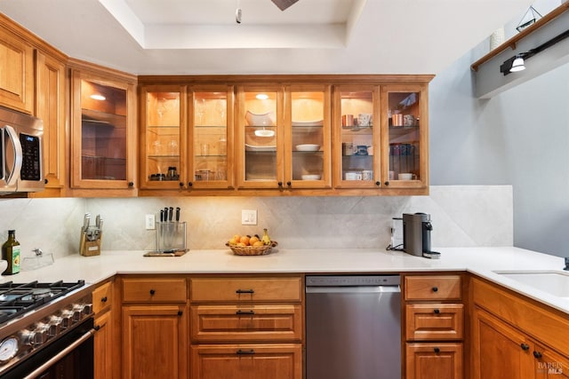 kitchen featuring brown cabinetry, stainless steel appliances, backsplash, and a tray ceiling