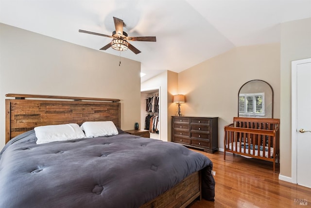 bedroom featuring a walk in closet, wood finished floors, a ceiling fan, and vaulted ceiling