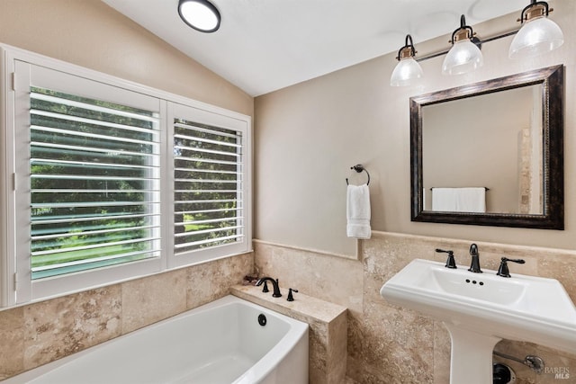 bathroom featuring tile walls, a wainscoted wall, a sink, a garden tub, and lofted ceiling