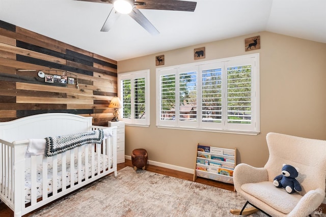 bedroom with a nursery area, baseboards, wooden walls, wood finished floors, and a ceiling fan
