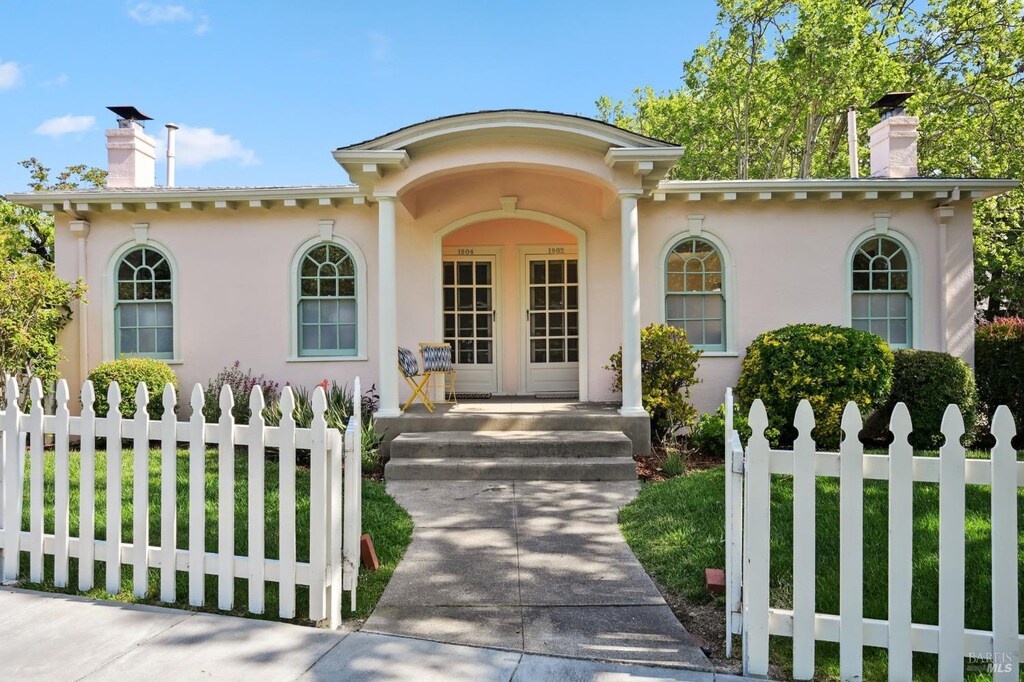 view of front of house with stucco siding, fence, and a chimney