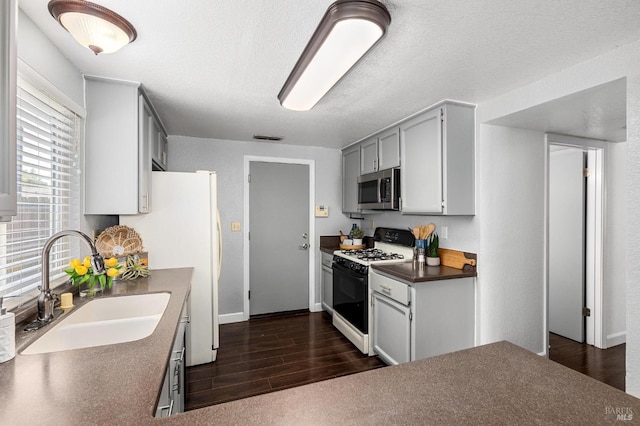 kitchen featuring stainless steel microwave, a sink, dark wood-style flooring, range with gas cooktop, and dark countertops