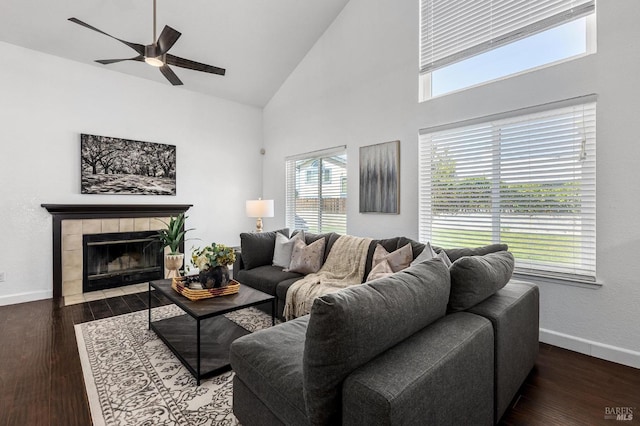 living area featuring a tiled fireplace, wood finished floors, ceiling fan, baseboards, and high vaulted ceiling