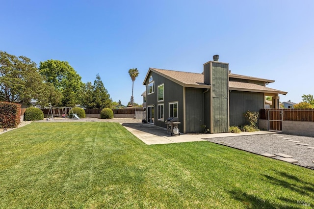 back of house featuring a chimney, a fenced backyard, a playground, and a lawn