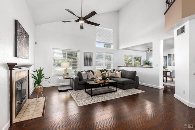 living area featuring ceiling fan, visible vents, wood-type flooring, a tiled fireplace, and high vaulted ceiling