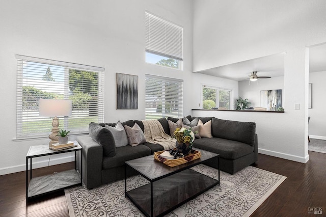 living area featuring baseboards, wood finished floors, ceiling fan, and a high ceiling