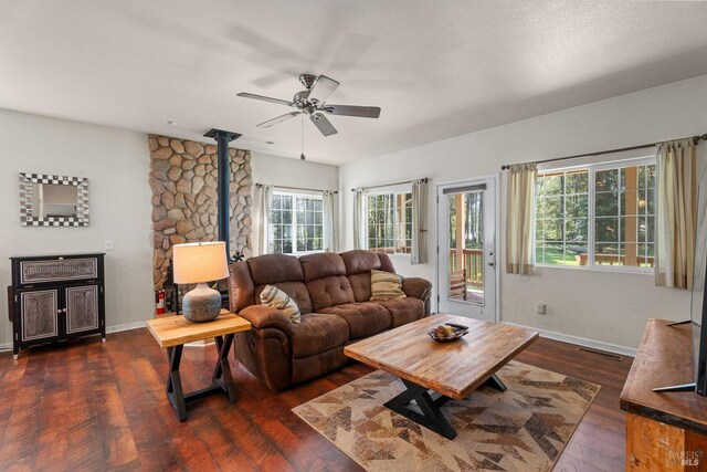 living room with dark wood-style floors, a wood stove, ceiling fan, visible vents, and baseboards
