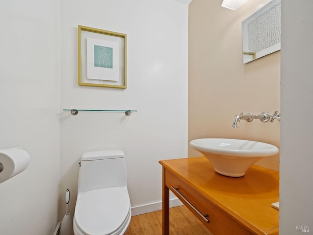 half bathroom featuring wood finished floors, toilet, and vanity