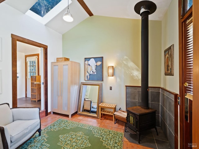 living area featuring lofted ceiling with skylight, a wood stove, wainscoting, and tile patterned floors