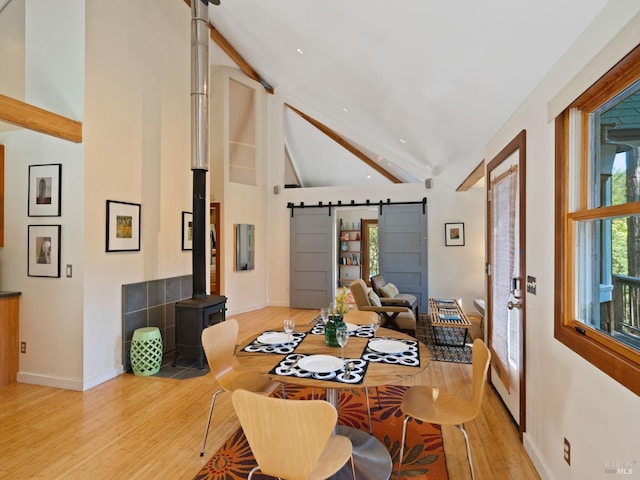dining room with light wood finished floors, beam ceiling, a barn door, high vaulted ceiling, and baseboards