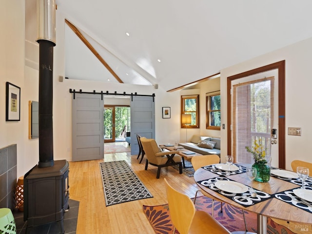 dining area with wood finished floors, a barn door, beamed ceiling, and a wood stove
