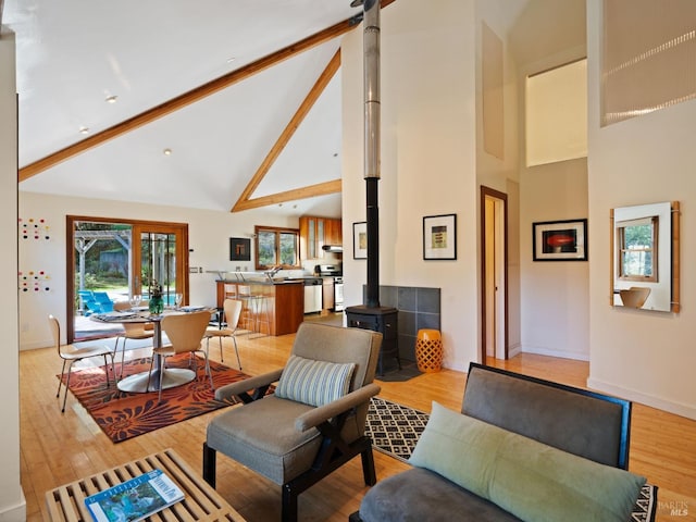 living area with a wood stove, high vaulted ceiling, baseboards, and light wood-type flooring