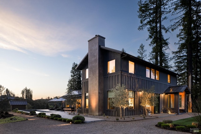 view of side of home with board and batten siding, a chimney, and a patio area