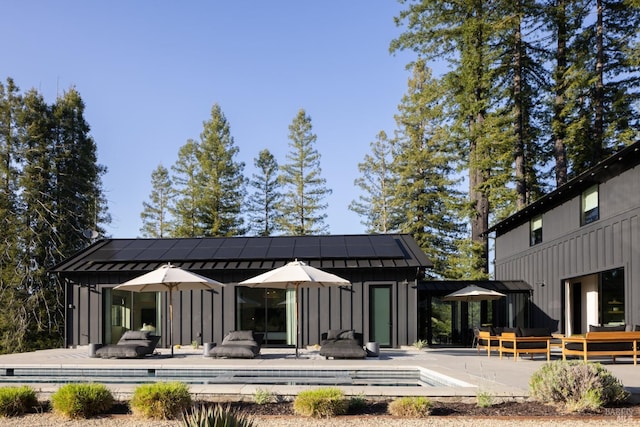back of house with board and batten siding, an outbuilding, an outdoor pool, and an exterior structure