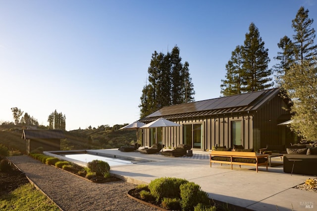back of property featuring an outdoor hangout area, a patio, board and batten siding, and roof mounted solar panels