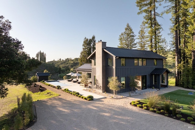 view of front facade featuring a patio, a standing seam roof, a chimney, and metal roof