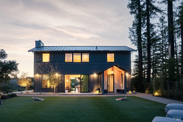 back of property with a lawn, a standing seam roof, and a chimney