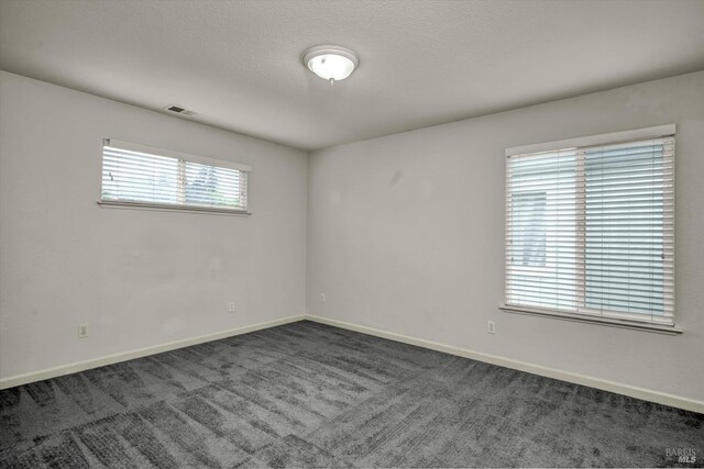 spare room with a textured ceiling, visible vents, dark colored carpet, and baseboards