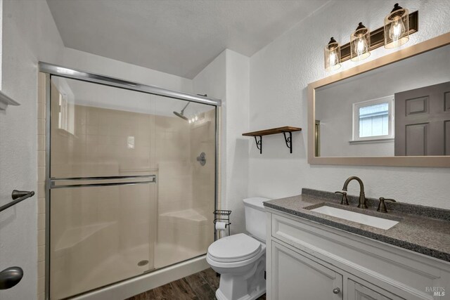 bathroom with a shower stall, vanity, toilet, a textured wall, and wood finished floors