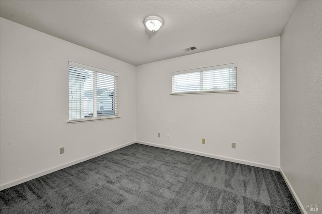 empty room featuring visible vents, dark carpet, and plenty of natural light