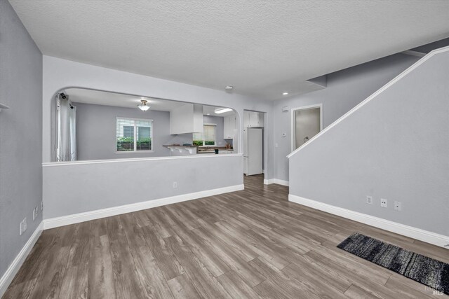 unfurnished living room with a textured ceiling, stairway, baseboards, arched walkways, and wood finished floors