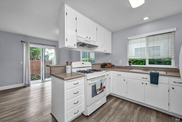 kitchen with white cabinets, a sink, white range with gas stovetop, under cabinet range hood, and a peninsula