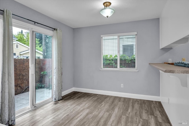 unfurnished dining area featuring light wood-style floors, plenty of natural light, and baseboards
