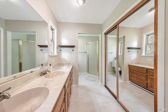 full bathroom with a stall shower, double vanity, a sink, and baseboards