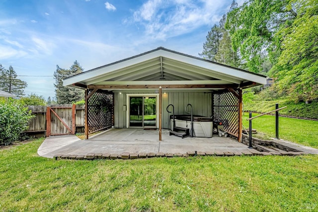 back of property with a yard, a gate, fence, a hot tub, and a patio
