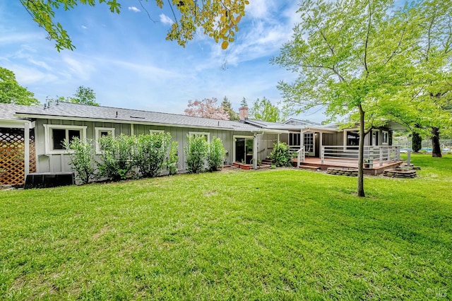 rear view of property featuring board and batten siding, a wooden deck, a sunroom, and a lawn