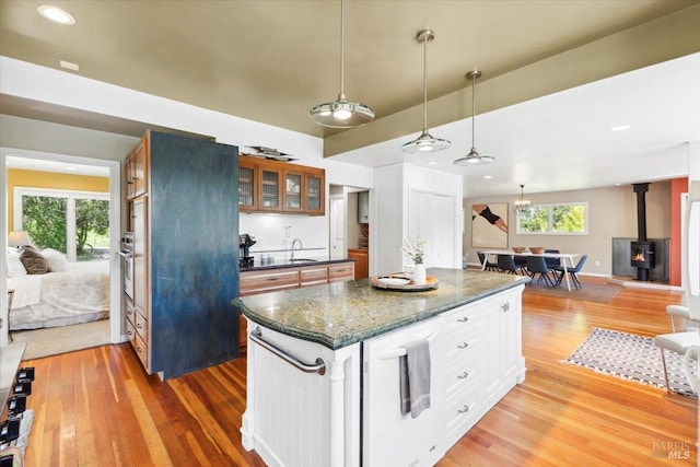 kitchen with glass insert cabinets, light wood-style flooring, a sink, white cabinetry, and a wood stove
