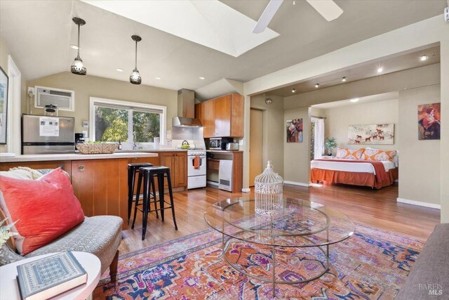 interior space with baseboards, a wall mounted air conditioner, vaulted ceiling with skylight, and light wood-style flooring