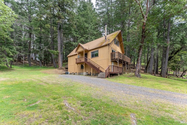 exterior space featuring a shingled roof, a wooden deck, stairs, and a front lawn