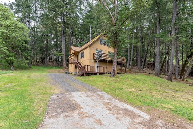 exterior space featuring a front yard, a wooden deck, a wooded view, gravel driveway, and stairs