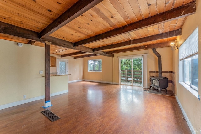 unfurnished living room featuring visible vents, a wood stove, wood finished floors, and beamed ceiling