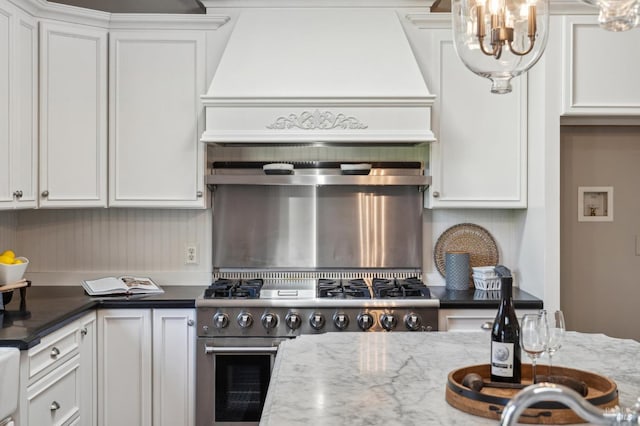 kitchen featuring stainless steel range, a notable chandelier, dark stone countertops, and white cabinets
