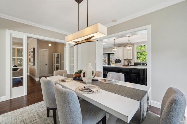dining space featuring dark wood-type flooring, crown molding, and baseboards