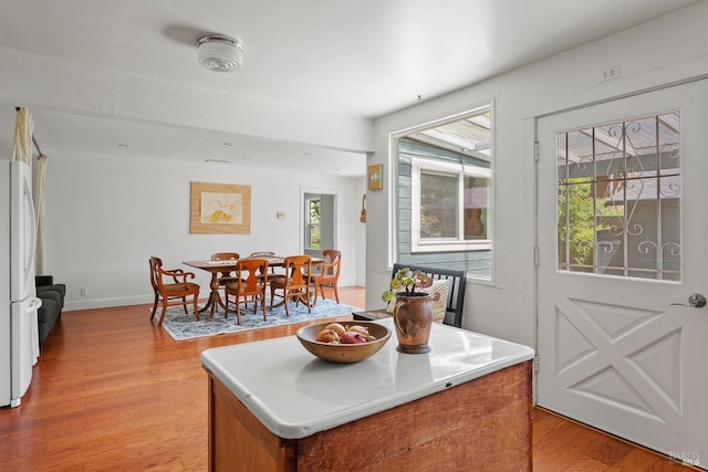 kitchen featuring freestanding refrigerator, brown cabinetry, light wood-style floors, baseboards, and a center island