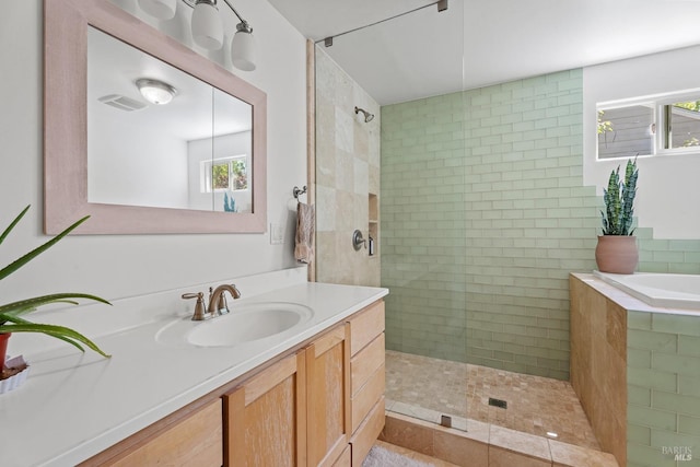 bathroom with a tile shower, vanity, a washtub, and visible vents