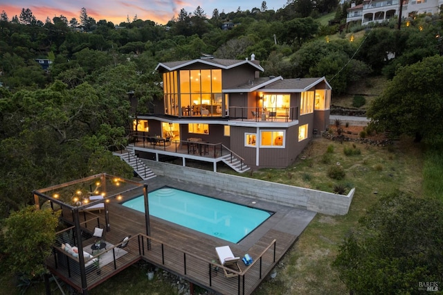 back of property at dusk featuring a fenced in pool, a deck, stairs, and a balcony