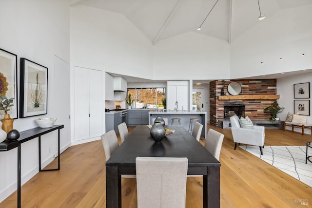 dining space featuring high vaulted ceiling, light wood-style flooring, and a brick fireplace