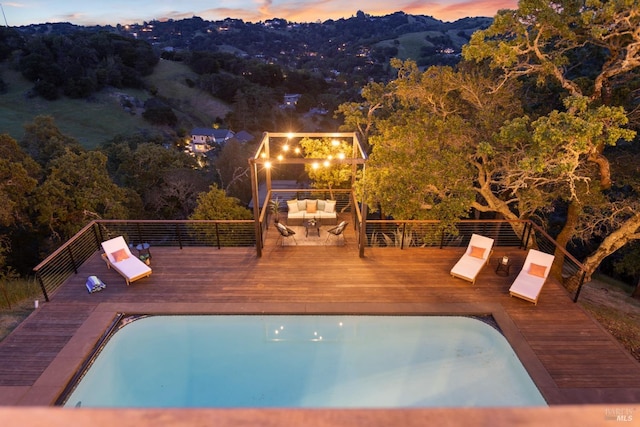 pool at dusk featuring a deck, an outdoor hangout area, and an outdoor pool