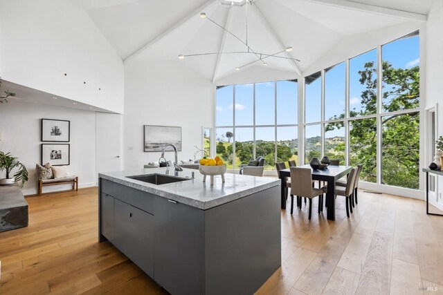 kitchen featuring modern cabinets, a sink, high vaulted ceiling, a center island with sink, and light wood-style flooring