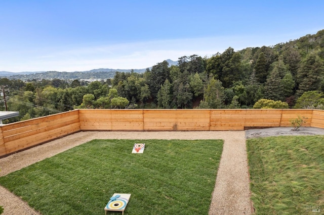 view of yard with a fenced backyard, a view of trees, and a mountain view
