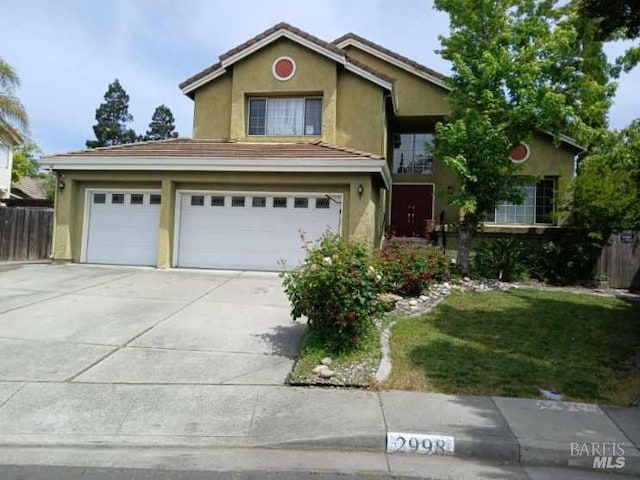 traditional-style house featuring concrete driveway, an attached garage, fence, and stucco siding