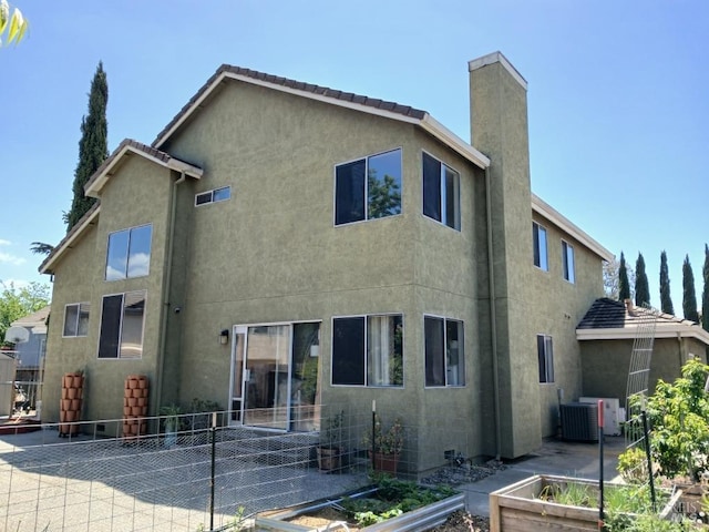 rear view of house with fence, stucco siding, a vegetable garden, a chimney, and a patio area