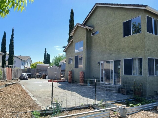 back of house featuring a storage shed, stucco siding, a vegetable garden, an outbuilding, and a patio area