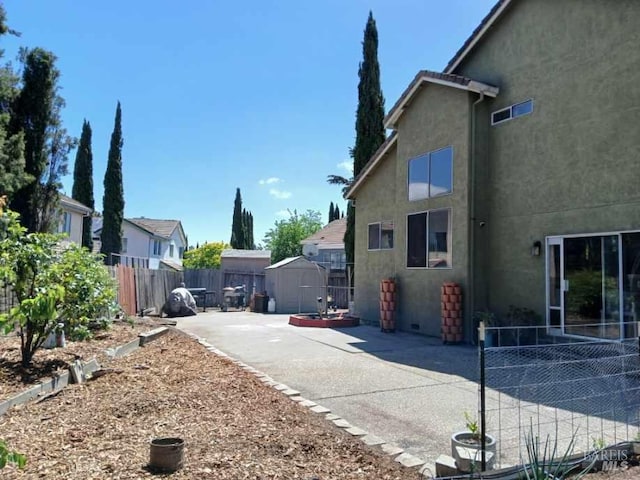 view of side of property with fence, stucco siding, a shed, a patio area, and an outbuilding