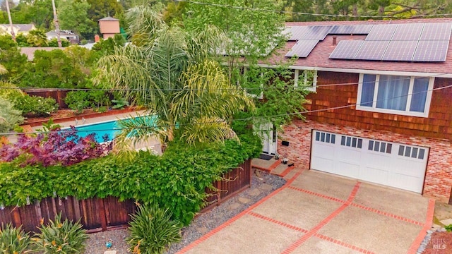 exterior space featuring brick siding, an attached garage, fence, and solar panels
