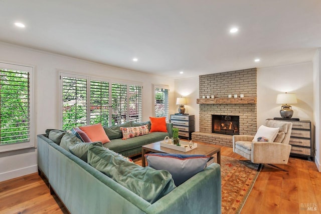 living area featuring crown molding, a brick fireplace, hardwood / wood-style floors, recessed lighting, and baseboards